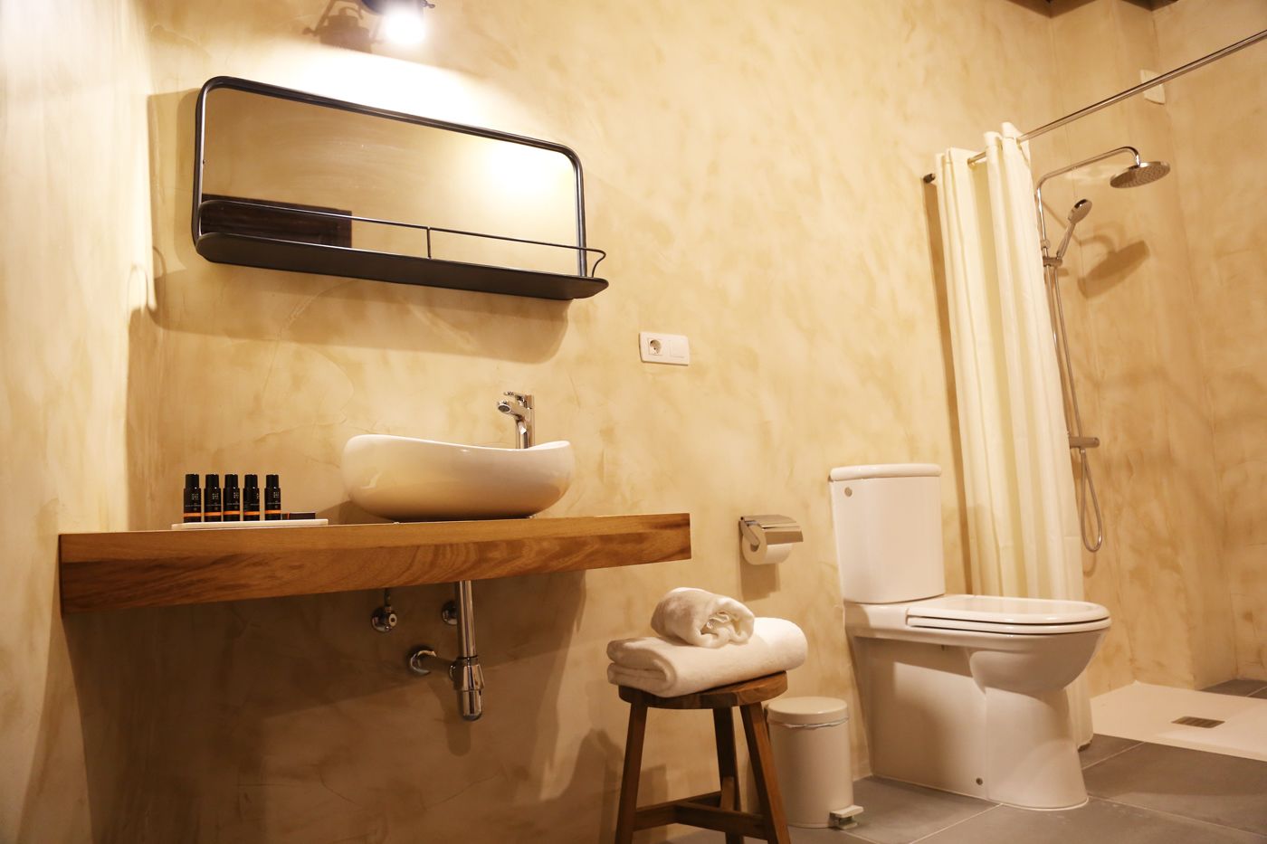 Un baño con tocador de madera, lavamanos sobre encimera, inodoro y ducha.