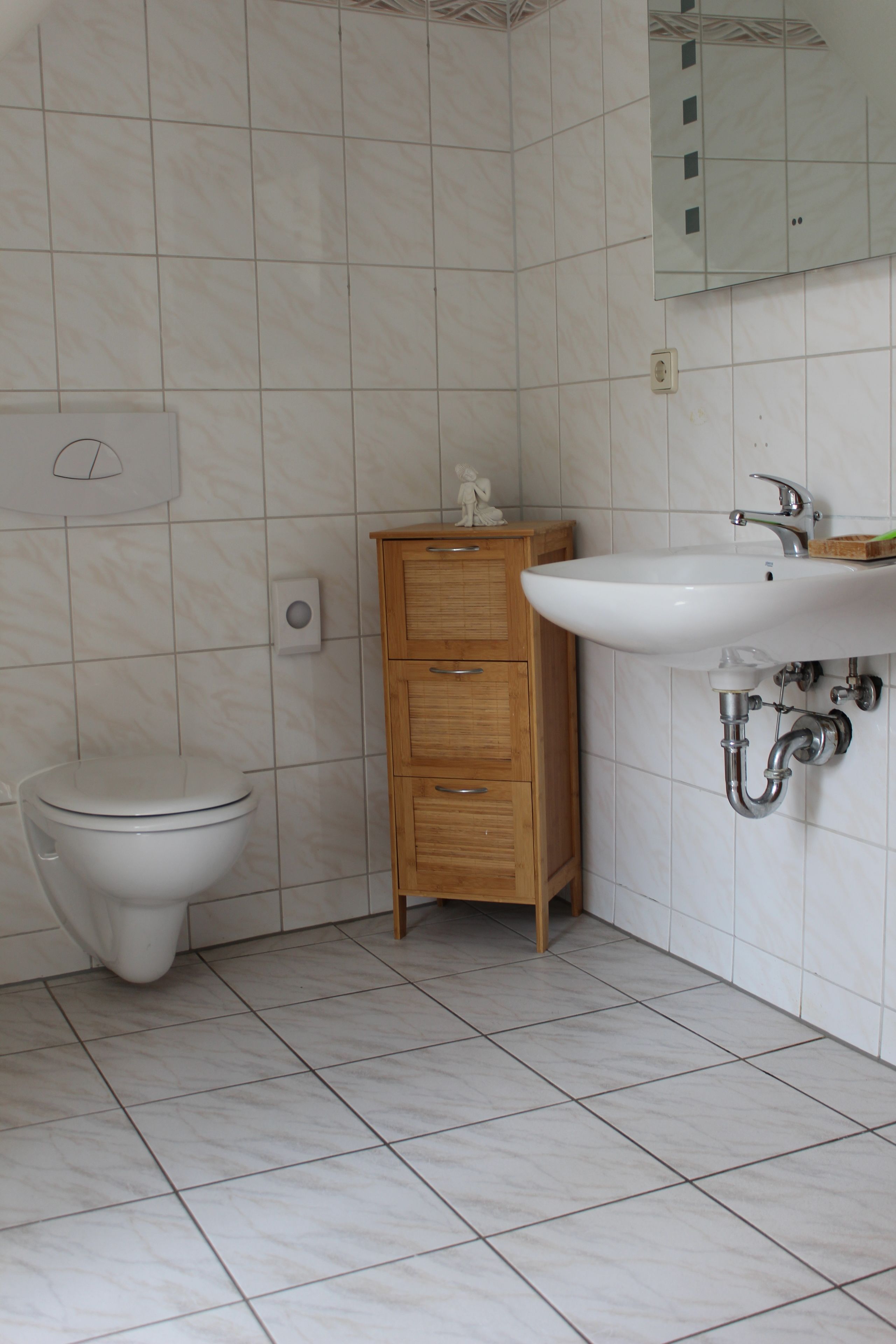 A bathroom with a toilet, wooden cabinet, and a sink with a mirror above it.