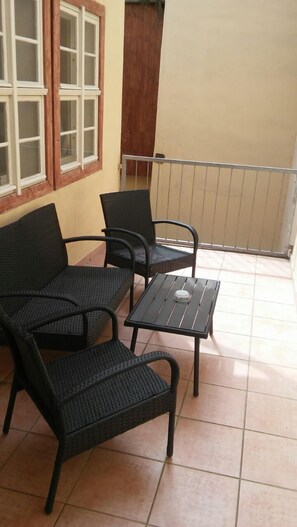 A balcony with two black wicker chairs and a small table, a wooden door, and a window with white frames. - Appartments am Brunnen (Quedlinburg)