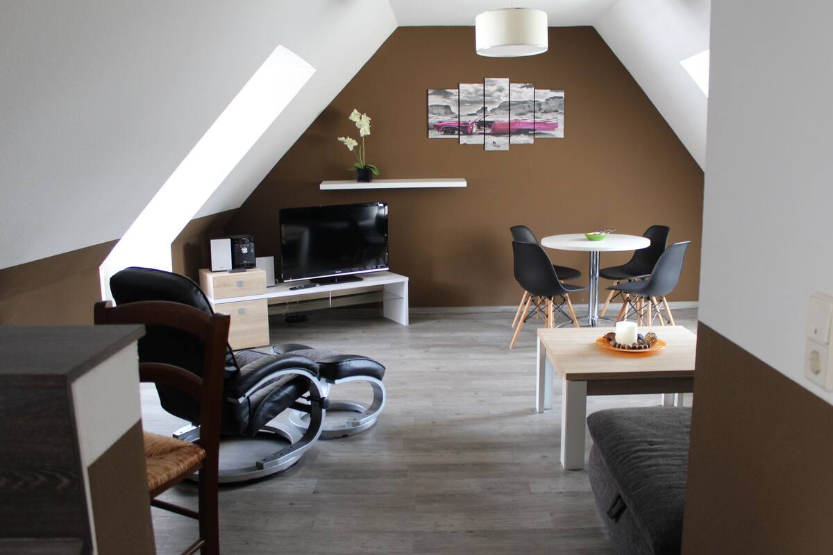 A modern loft apartment with a dining area, a seating area, and a TV.