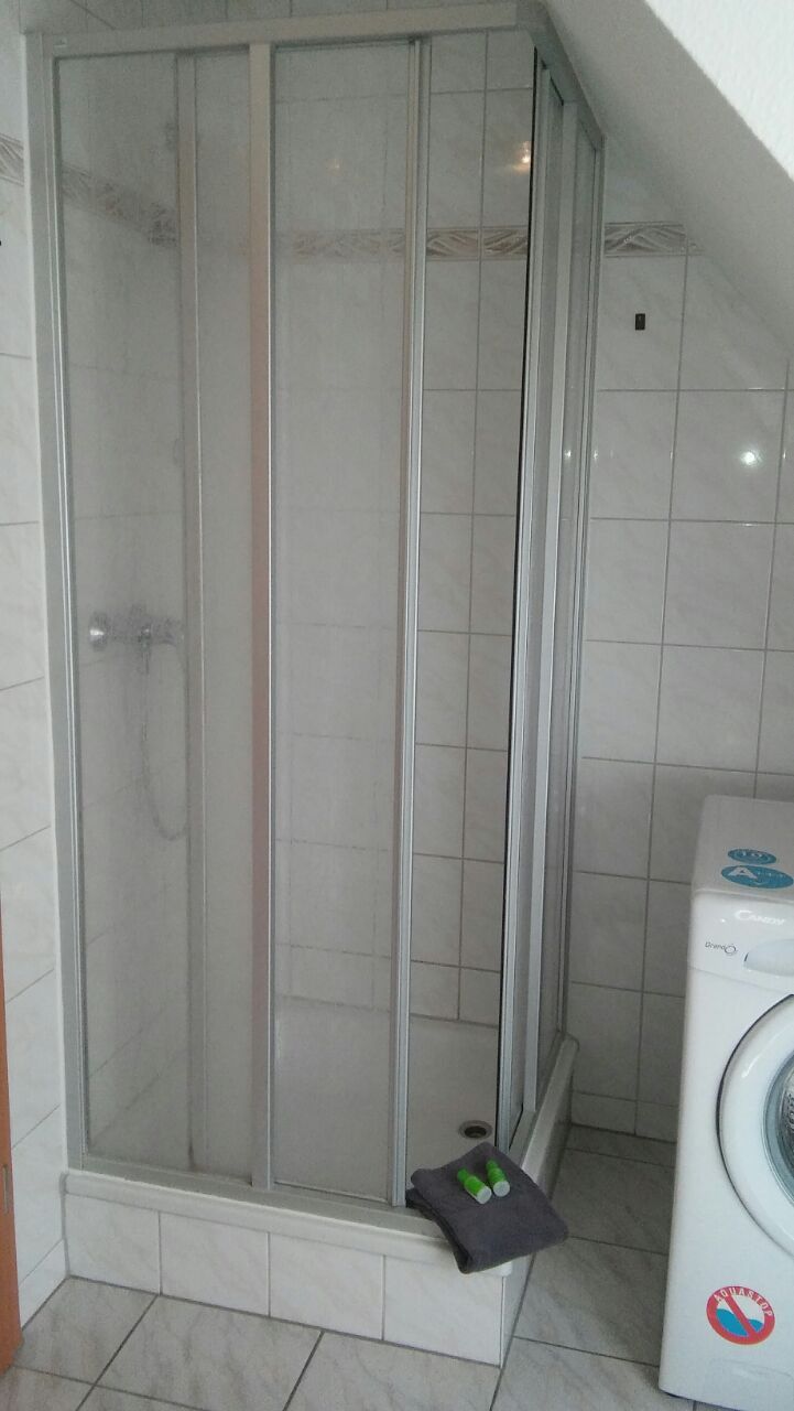 Une cabine de douche avec une porte en verre, un porte-serviettes avec une serviette et un lave-linge.