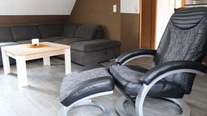 Un salon moderne avec un canapé d’angle gris, une table basse en bois et un fauteuil en cuir noir doté d’un pied circulaire.