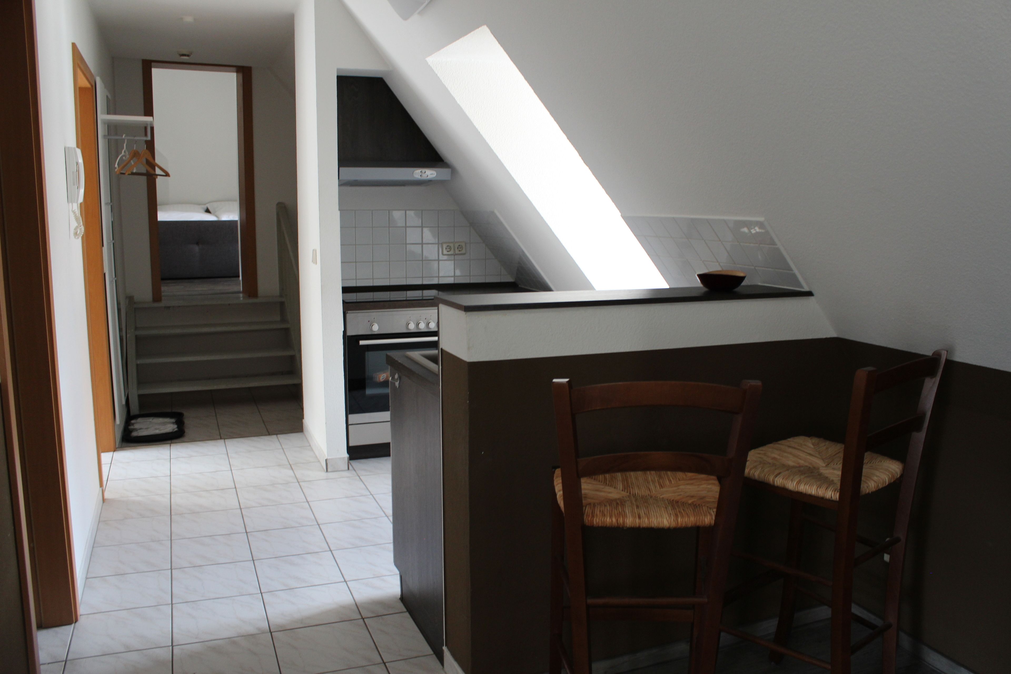 A compact kitchen with a small dining area, a staircase leading to a bedroom, and a skylight above the counter.