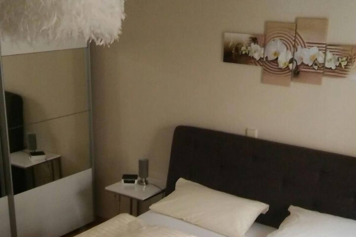 A hotel room with a large bed, a bedside table with a lamp, a mirror, and a wall art piece.
