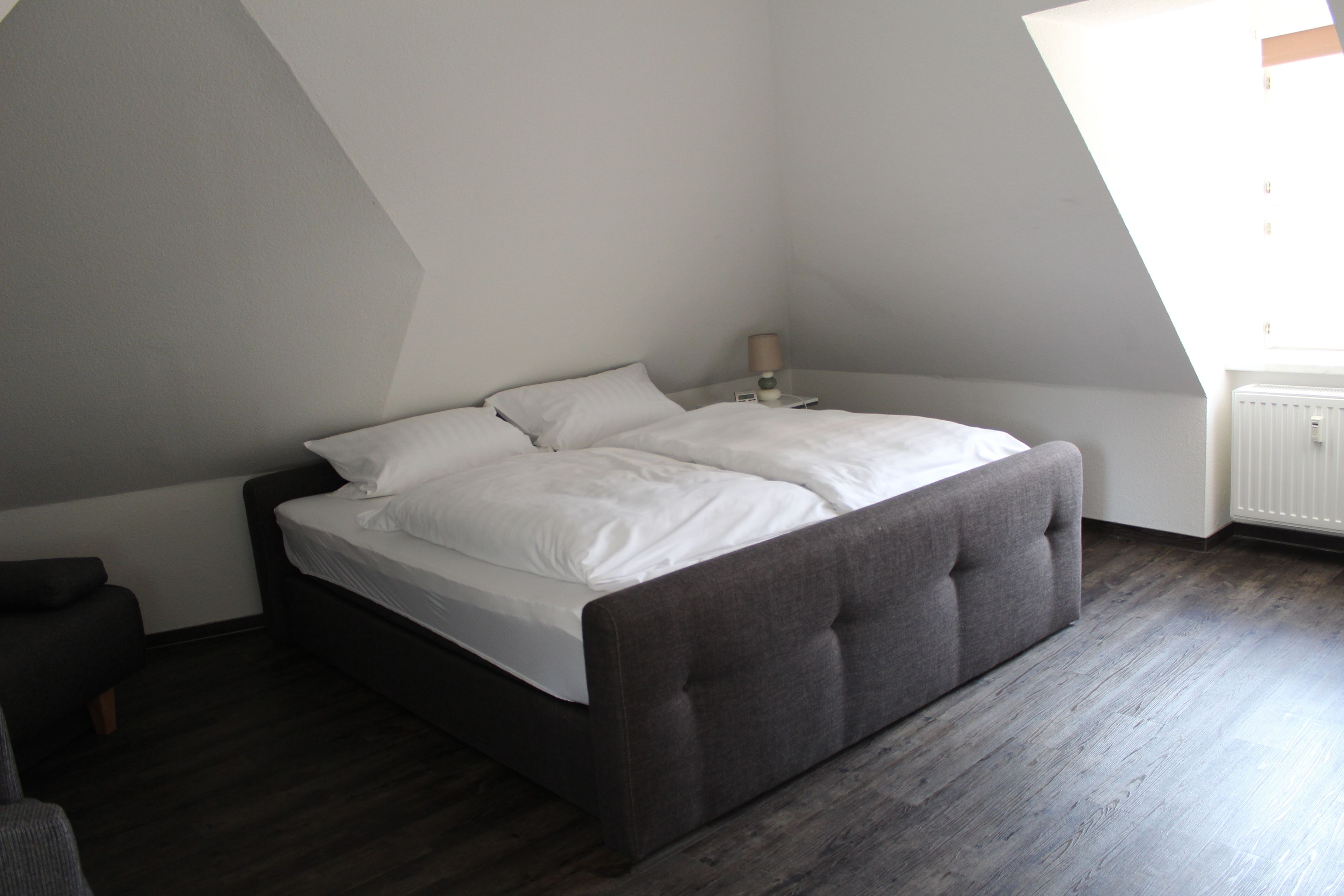 Un dormitorio con cama, mesita de noche, lámpara y radiador.