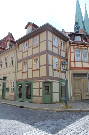 A traditional half-timbered building with a green door and windows, a cobblestone street, and a church steeple in the background. - Appartments am Brunnen (Quedlinburg)