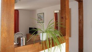 Een houten spiegel reflecteert een kamer met een potplant, een waterkoker en een televisie.