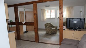 Een woonkamer met een bank, een televisie en een stoel. Er bevindt zich een houten balkenconstructie in het midden.