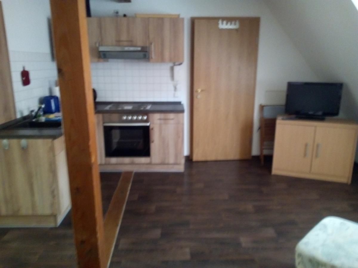 A compact kitchen with wooden cabinets, a stove, and a television on a small table.