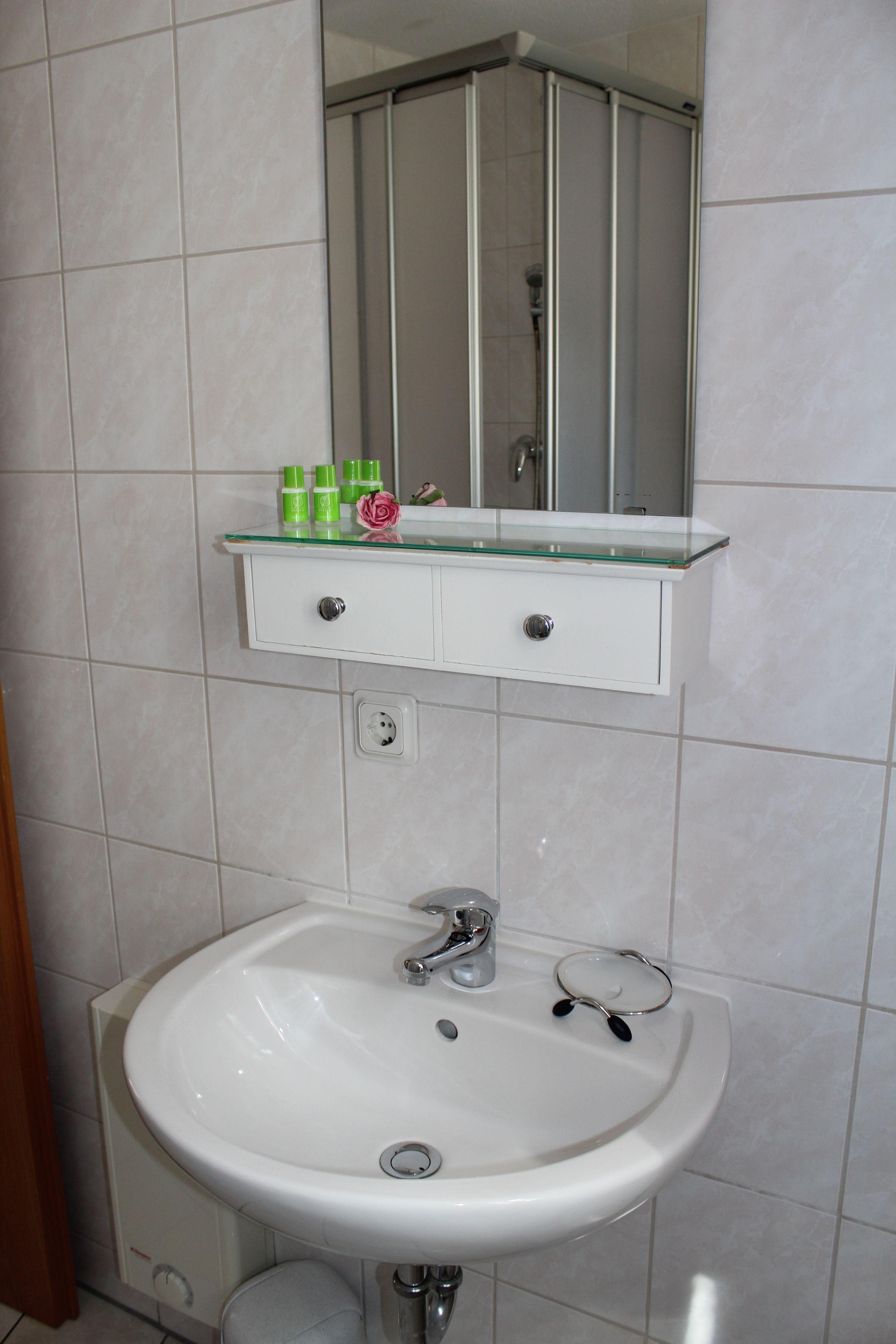 Un baño con un lavamanos blanco, una repisa de vidrio con artículos de aseo y un espejo sobre el lavamanos.