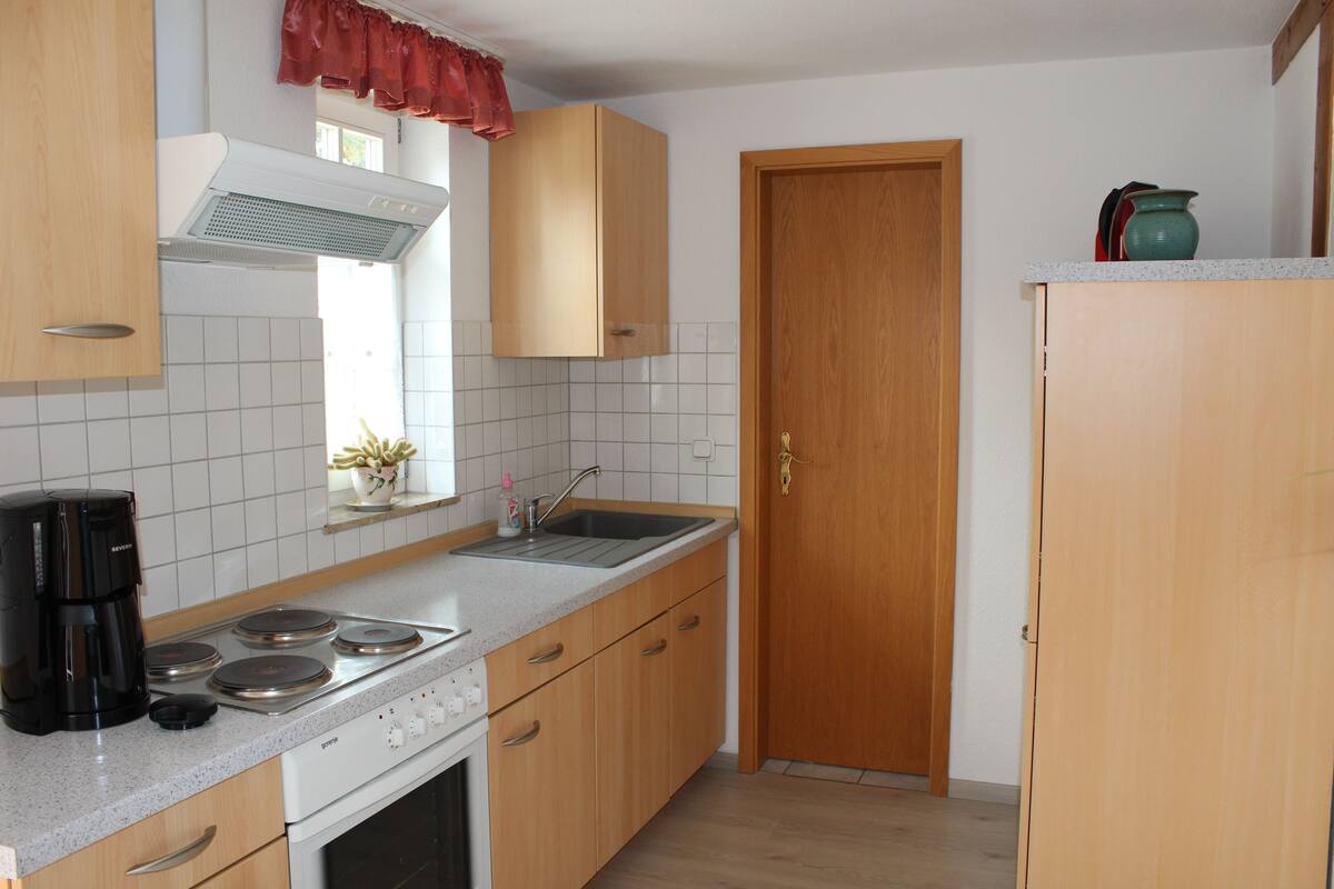 Een keuken met houten kastjes, een fornuis, een spoelbak en een raam met gordijnen.