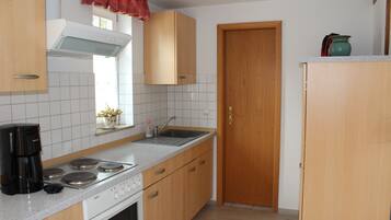Una cocina con armarios de madera, estufa, pileta y ventana con cortinas.
