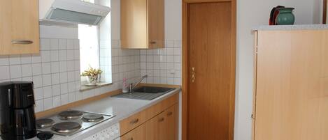 A kitchen with wooden cabinets, a stove, a sink, and a window with curtains.