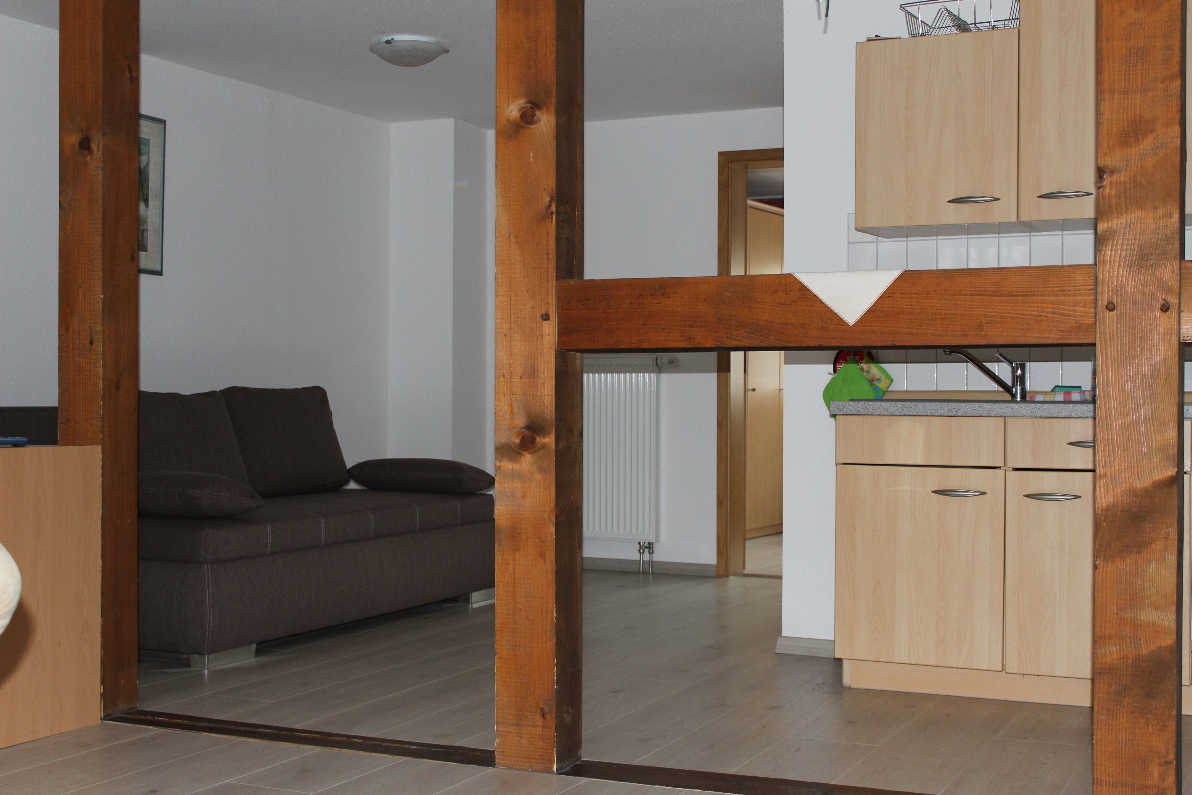 Ein modernes Wohnzimmer mit einer Couch, Holzbalken und einer Küchenzeile mit Holzausstattung.