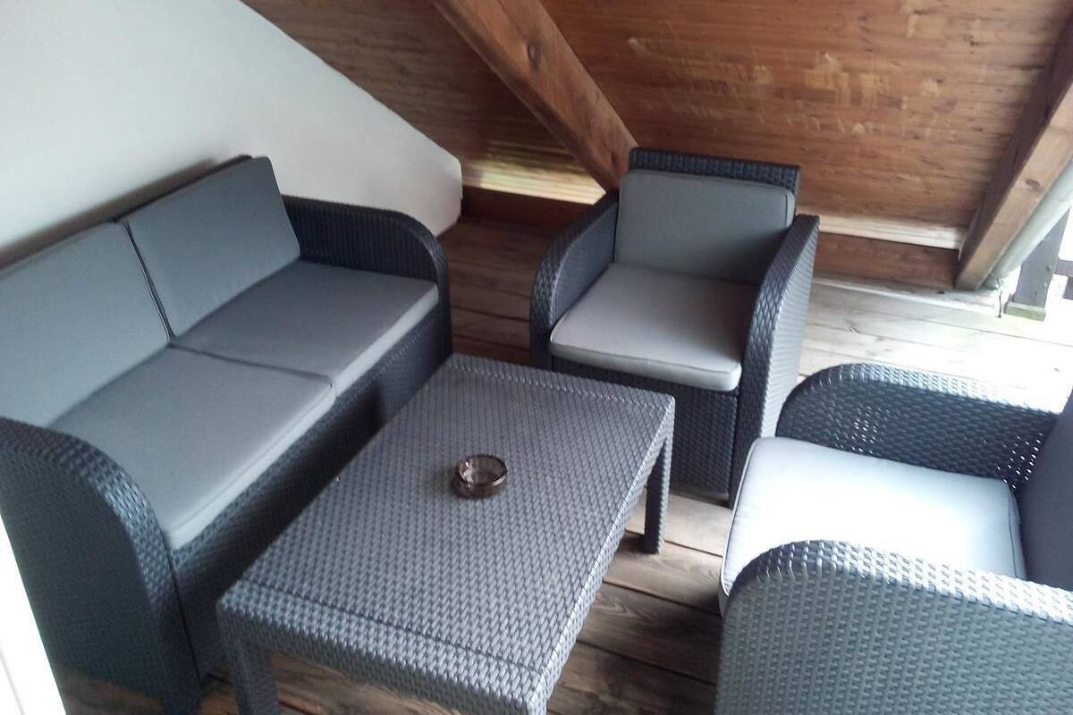 Een overdekte buitenruimte met een bank, twee stoelen en een tafel.