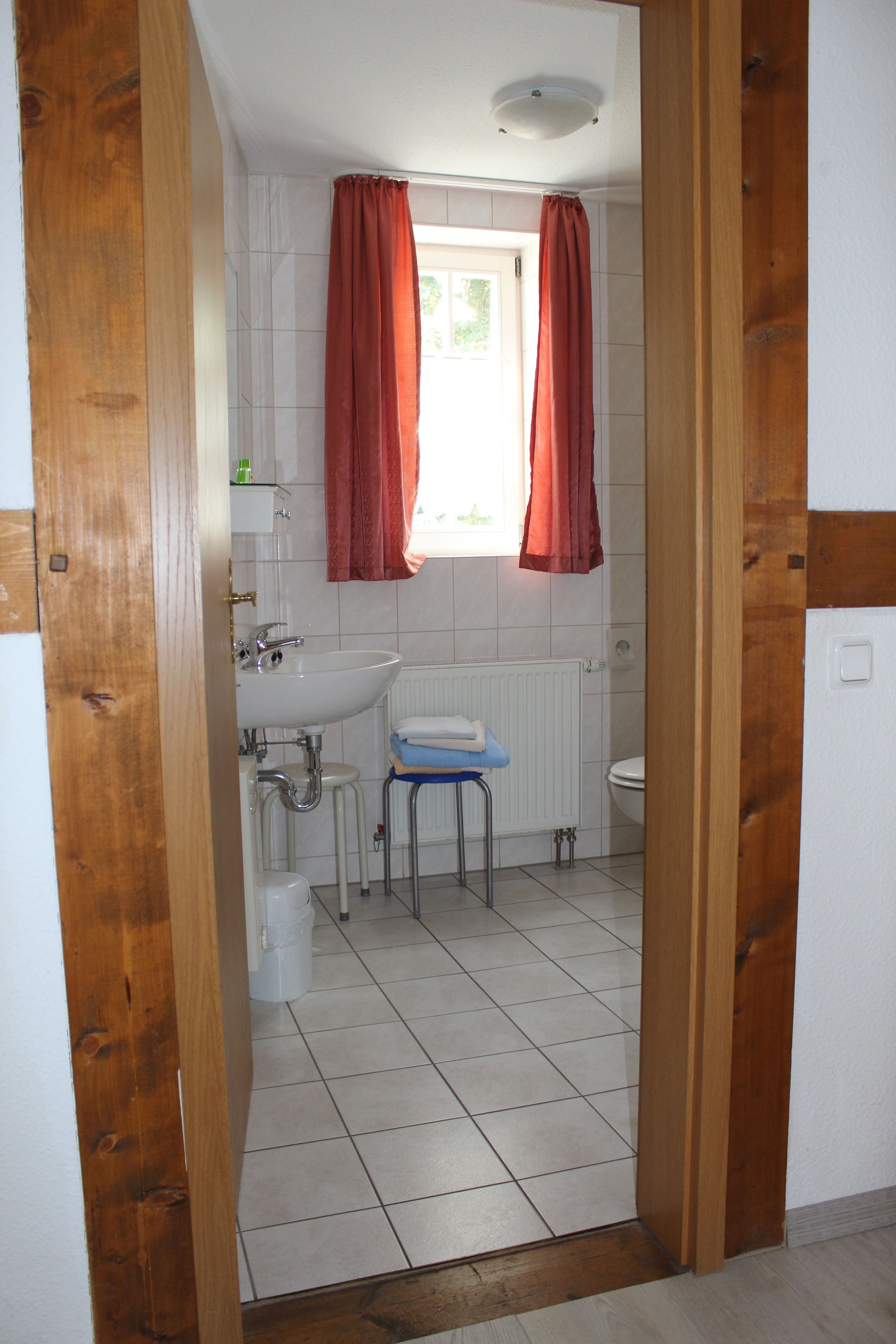 Une salle de bain avec un lavabo blanc, des toilettes et une fenêtre avec des rideaux rouges.
