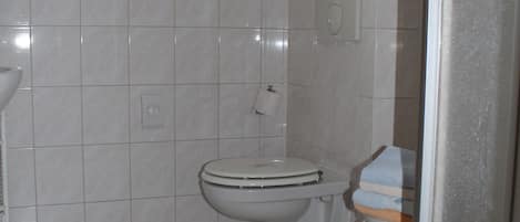 Un baño con paredes y suelo de azulejos blancos, un inodoro, un lavabo y un ventanal.