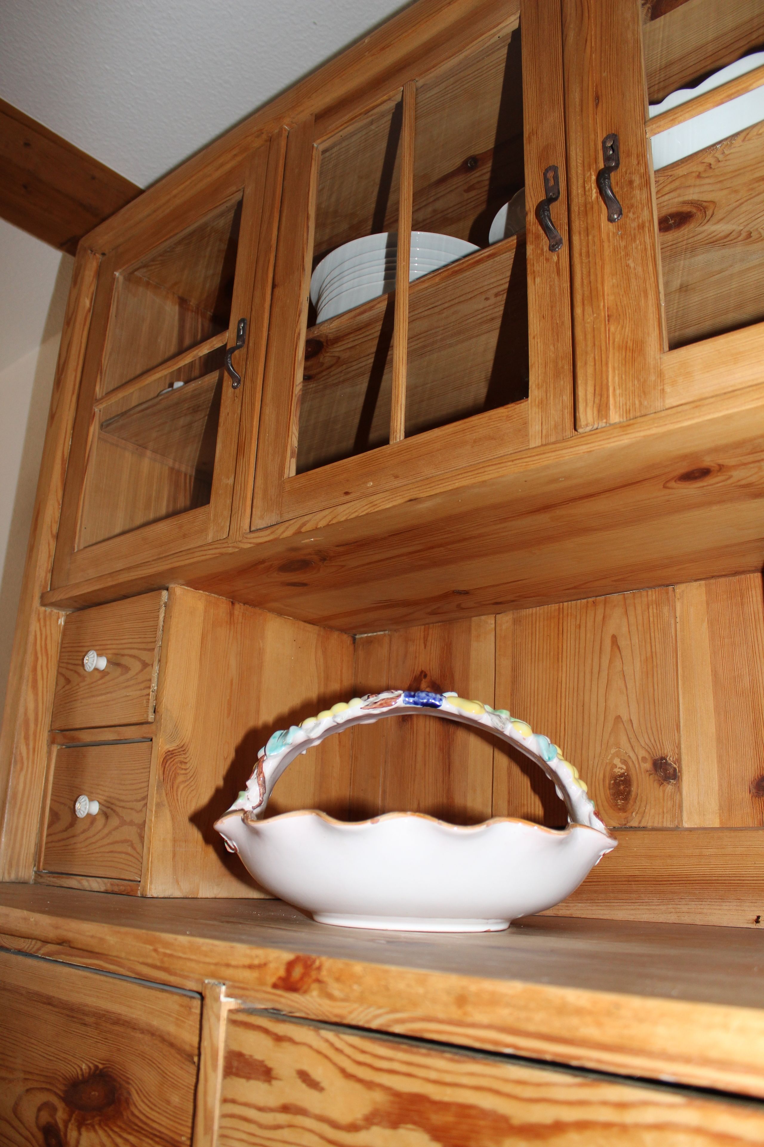 Un gabinete de madera con puertas de vidrio, un cuenco blanco y un cajón.