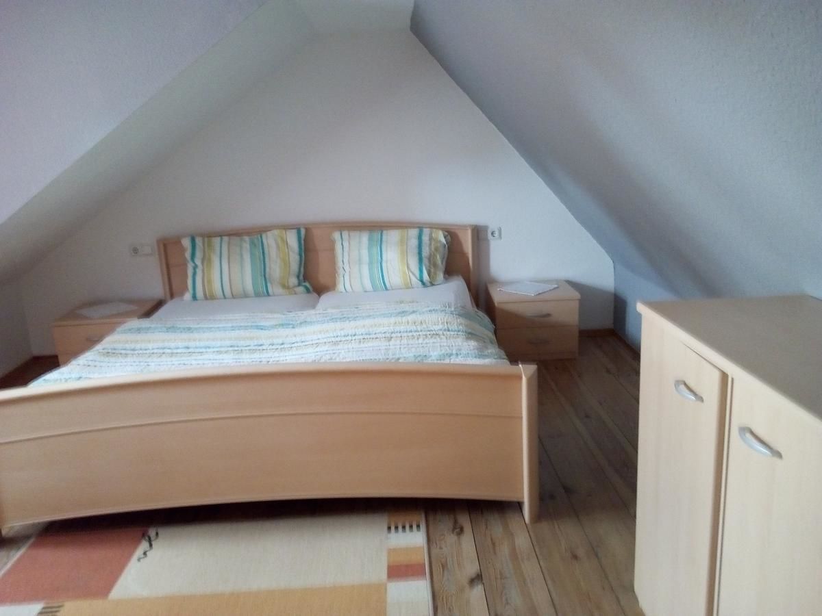 A bedroom with a sloped ceiling, a wooden bed with striped bedding, a nightstand, and a wooden wardrobe.