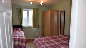 A bedroom with two beds, a wardrobe, a window with curtains, and a ceiling fan. - granary (London)