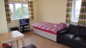 A room with a bed, a TV, a wooden table, a leather couch, and a window with curtains. - granary (London)