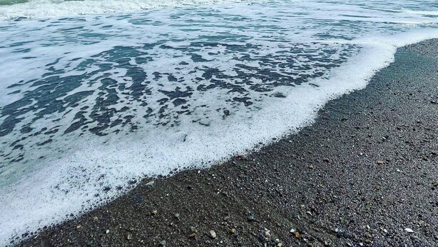 Ein Kiesstrand mit klarem Wasser und einem entfernten Berg.