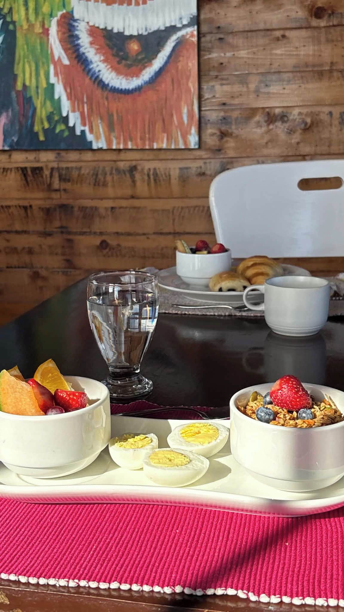 A breakfast setting with a glass of water, bowls of fruit, eggs, and a cup of coffee on a table.