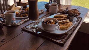 Ein Frühstückstisch mit Blick auf das Meer, mit Toast, Pfannkuchen, Kaffee und einem Schokoladengetränk.