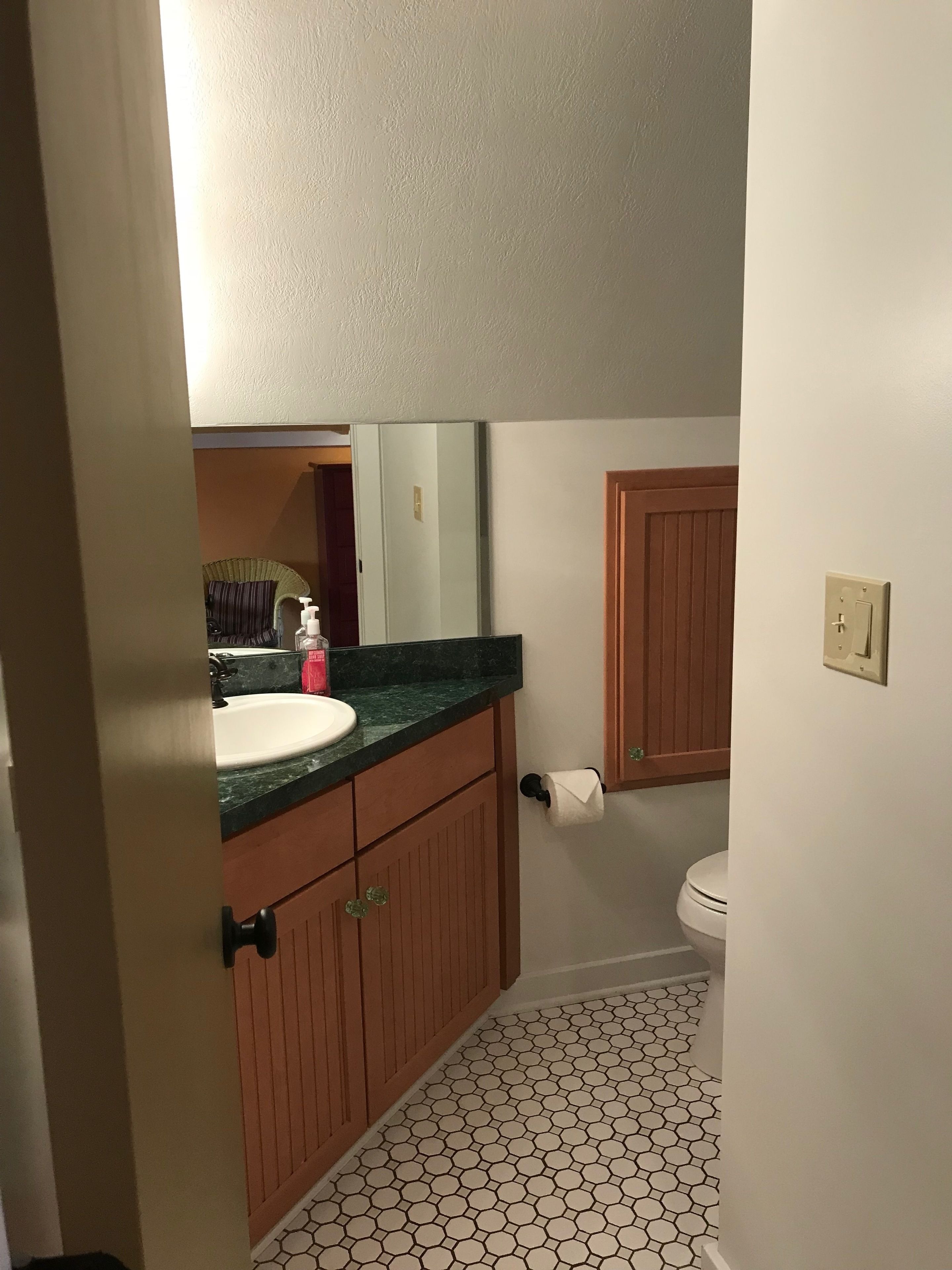 A bathroom with a white sink, wooden cabinets, a mirror, a toilet, and a patterned floor.