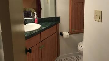 A bathroom with a white sink, wooden cabinets, a mirror, a toilet, and a patterned floor.