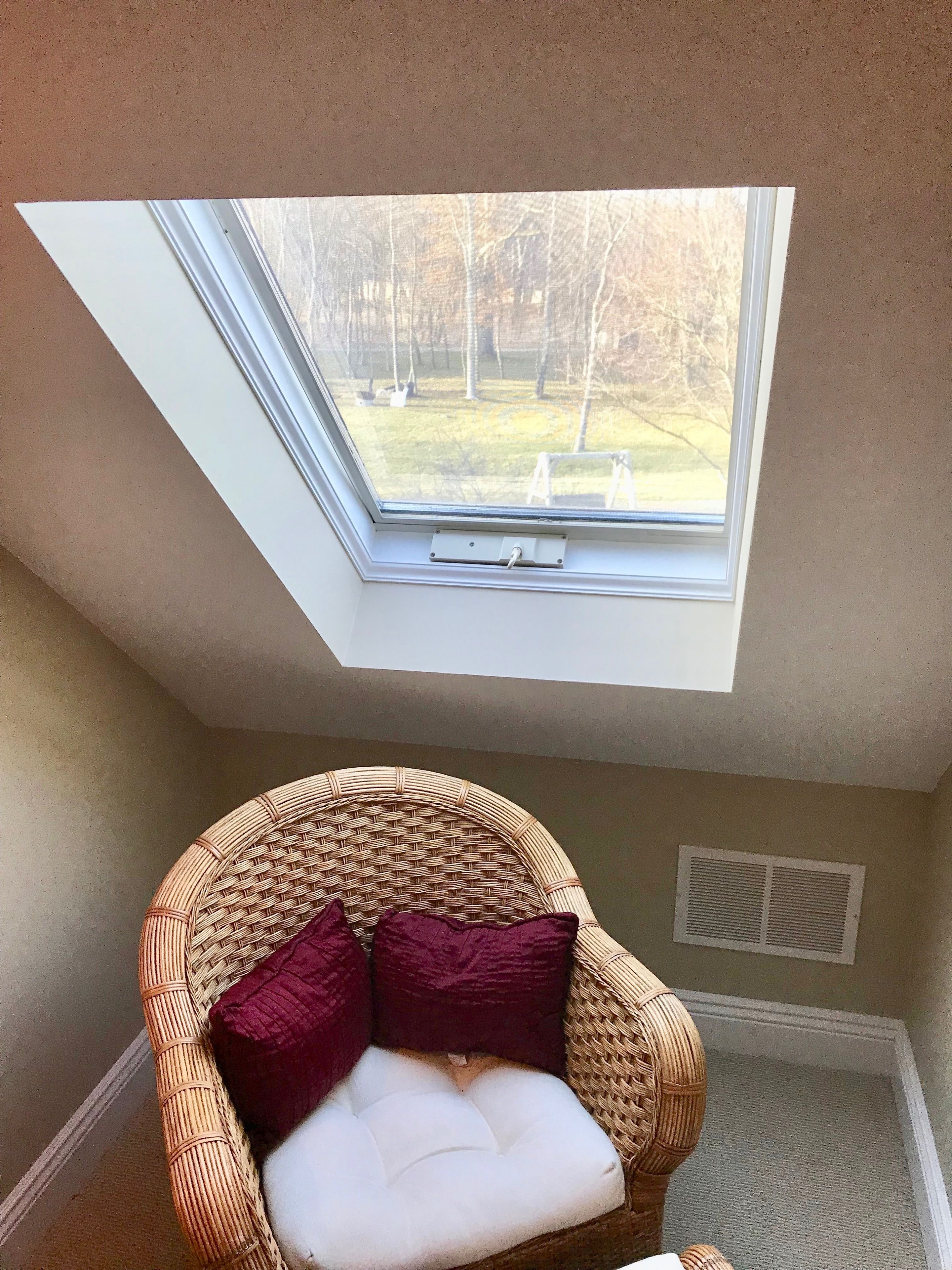 A room with a skylight, a wicker chair with cushions, and a radiator.
