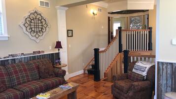 A living room with a plaid sofa, a wooden coffee table, a patterned armchair, a wooden staircase, and a decorative wall piece.