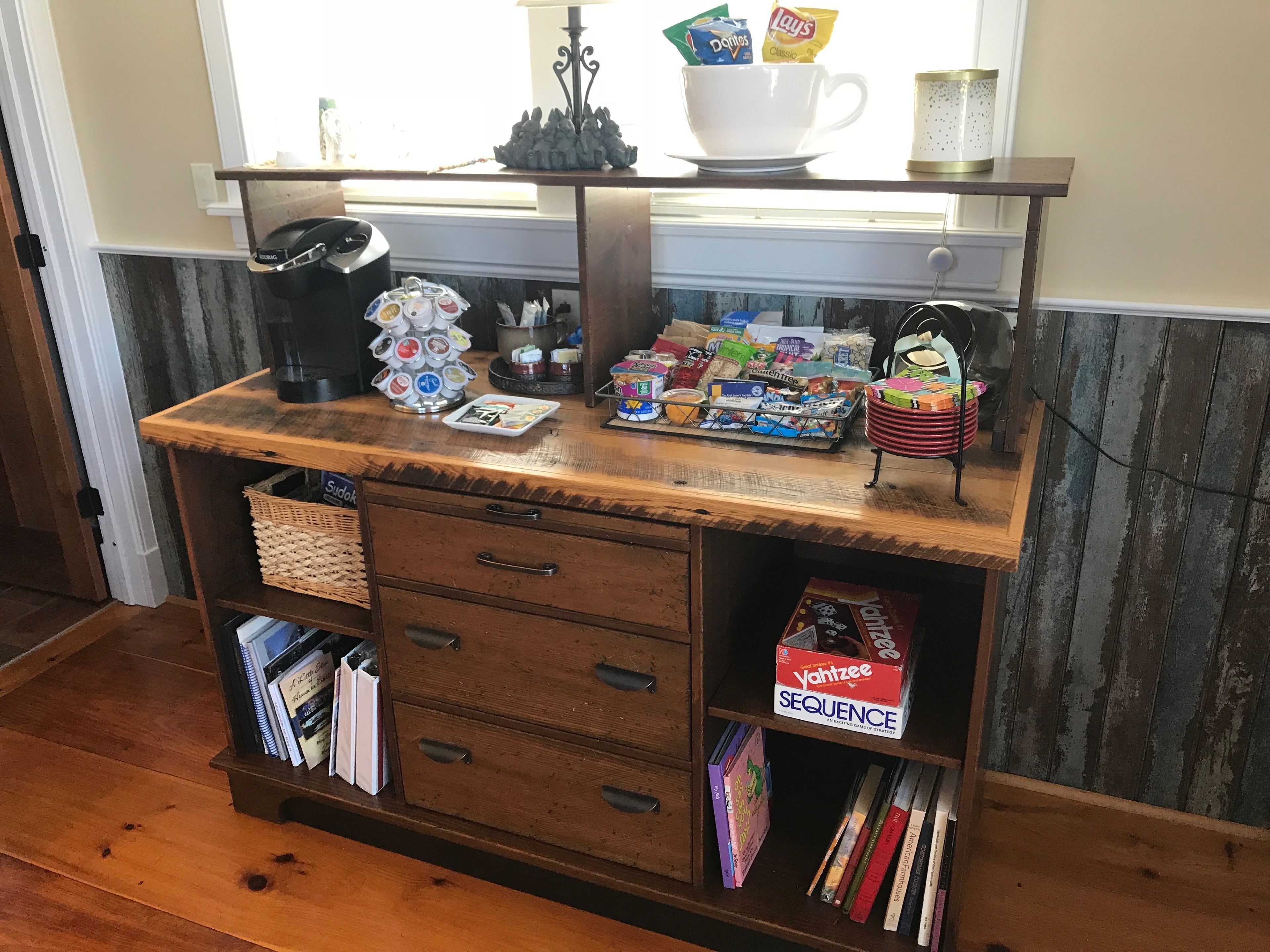 Escritorio de madera con cafetera, salero y pimentero, taza blanca, aperitivos y un juego de mesa.