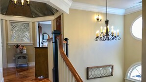 Un grand escalier avec une rampe en bois, un lustre orné de nombreuses bougies et un panneau décoratif mural.