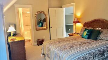 A bedroom with a large bed, a nightstand with a lamp, a mirror, and a ceiling fan.