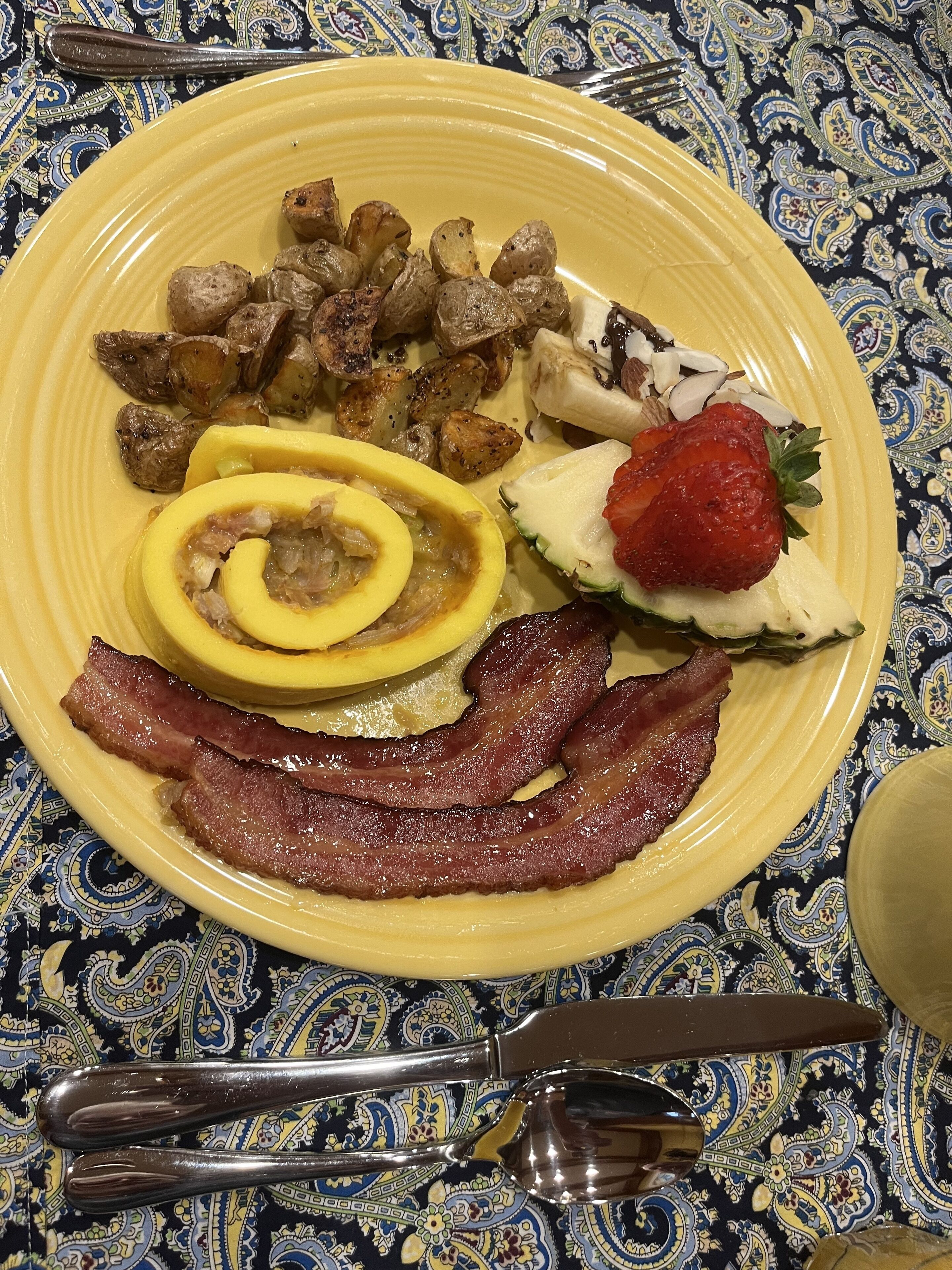A plate with bacon, eggs, potatoes, and a strawberry.