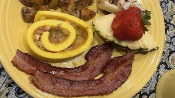 A plate with bacon, eggs, potatoes, and a strawberry.