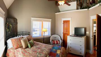 A bedroom with a bed, a dresser, a television, a window with blinds, and a ceiling fan.
