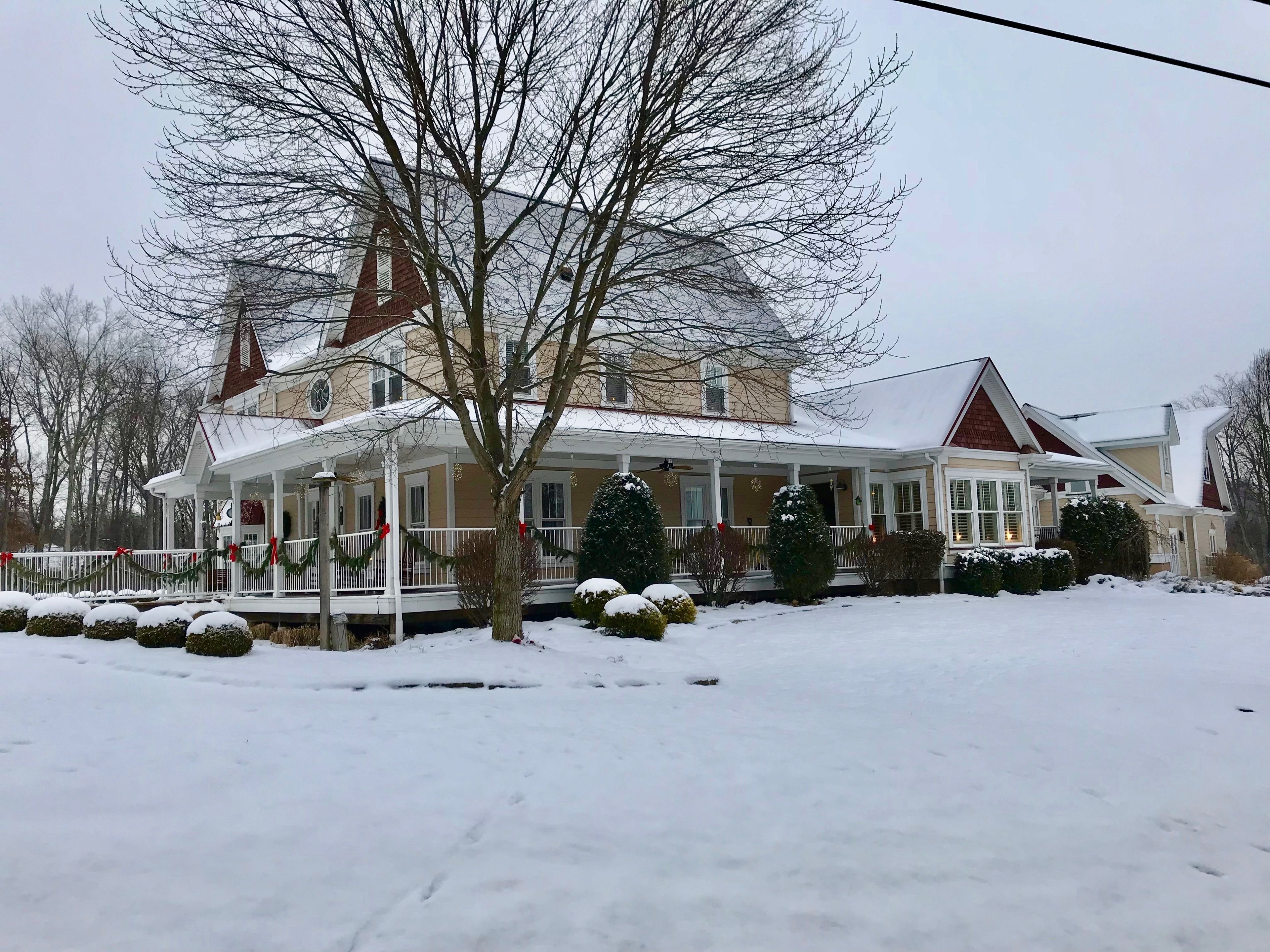 A large, two-story house with a wrap-around porch, surrounded by snow-covered ground and trees.