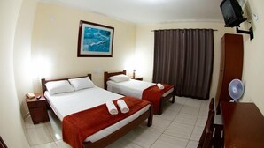 Ein Hotelzimmer mit zwei Betten, einem an der Wand befestigten Fernseher, einem Schreibtisch mit Stuhl und einem Fenster mit Vorhängen.