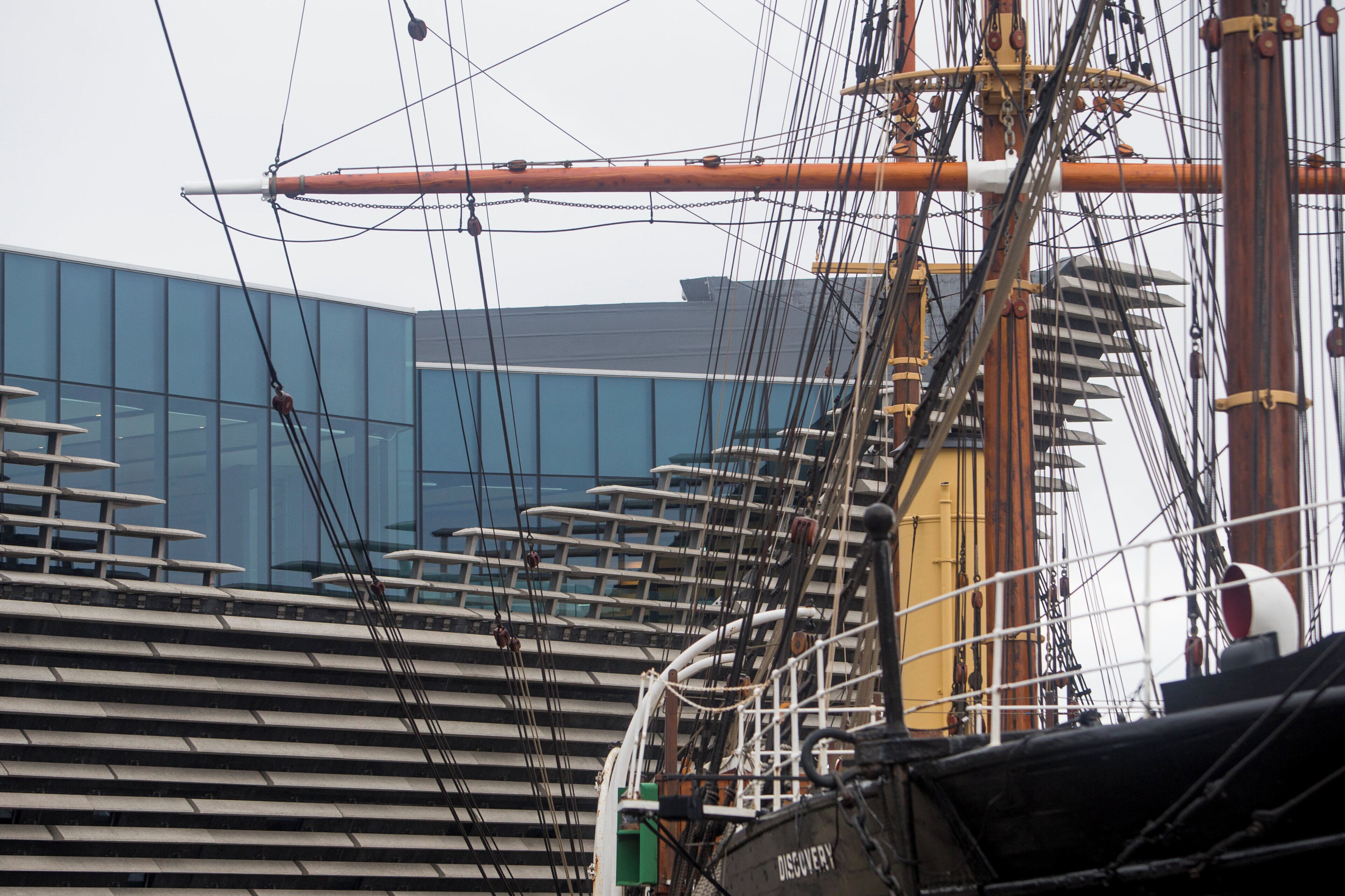 Arreglo de jarcia de barco y un edificio moderno al fondo.