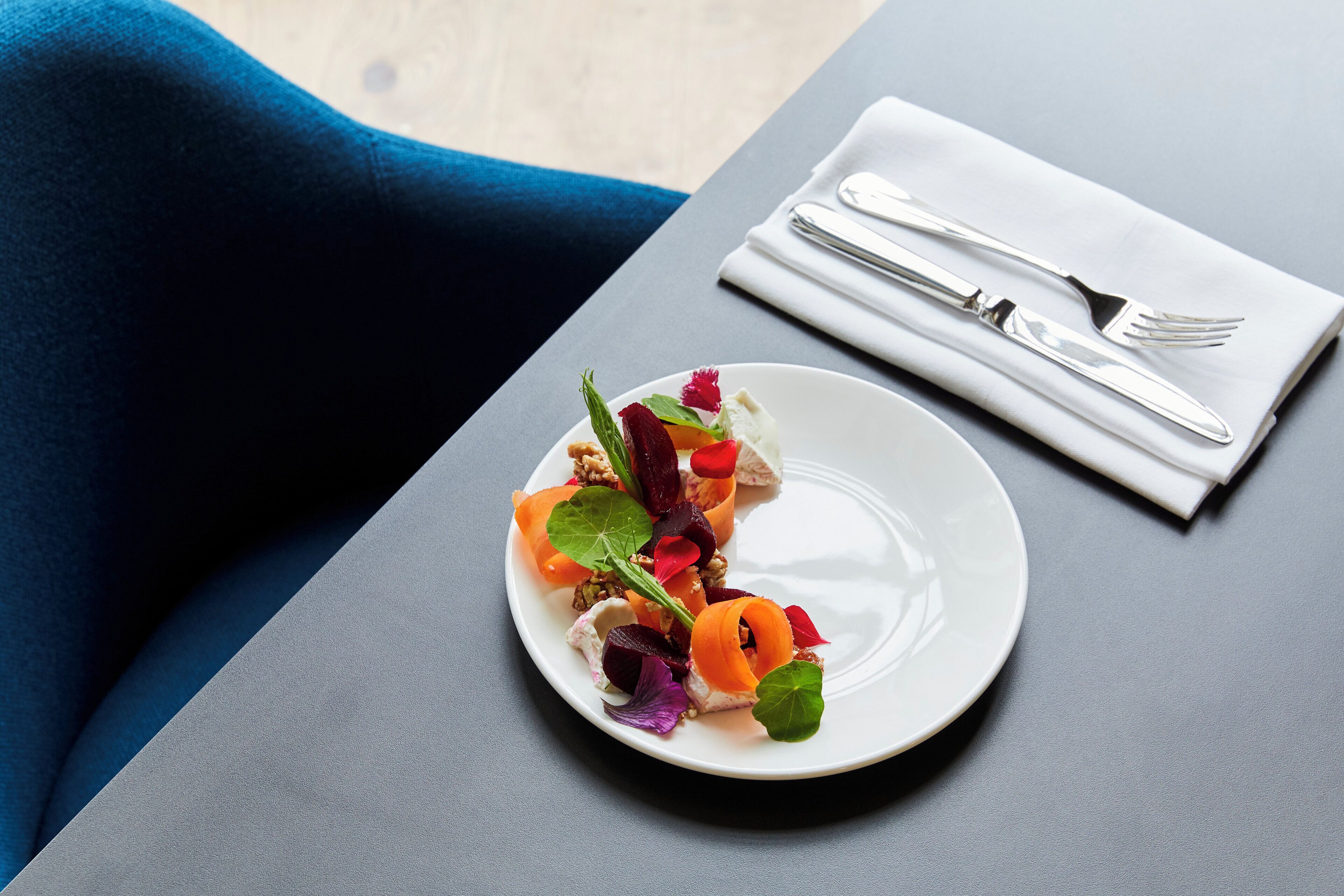 A white plate with a colorful salad on a dark table, accompanied by a white napkin and silverware.