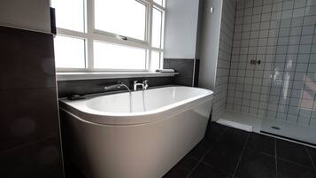 A modern bathroom with a freestanding bathtub, a window, and a tiled shower area.