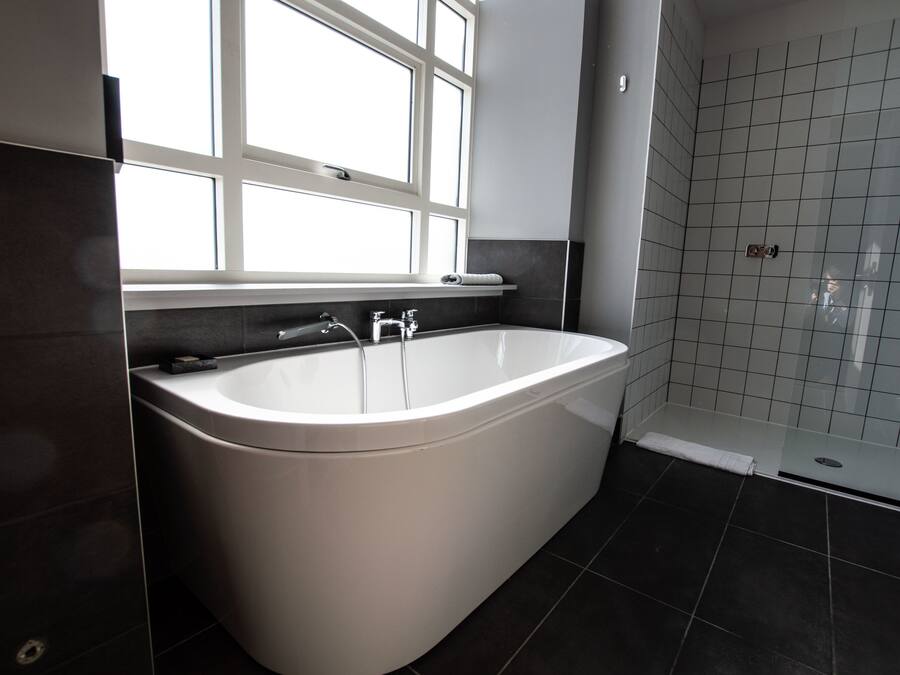 A modern bathroom with a freestanding bathtub, a window, and a tiled shower area.