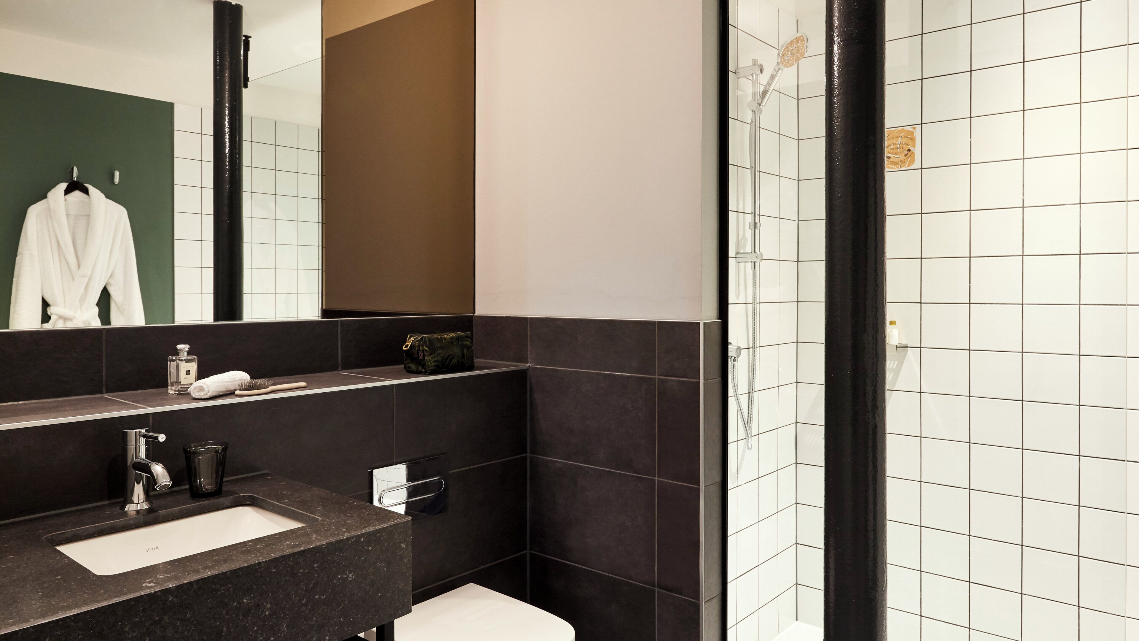 A modern bathroom with a dark tiled wall, a white sink, and a shower area.