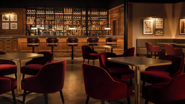 A bar area with multiple seating tables and red chairs, a well-stocked liquor shelf, and framed pictures on the walls. - Hotel Indigo Dundee by IHG (Dundee)