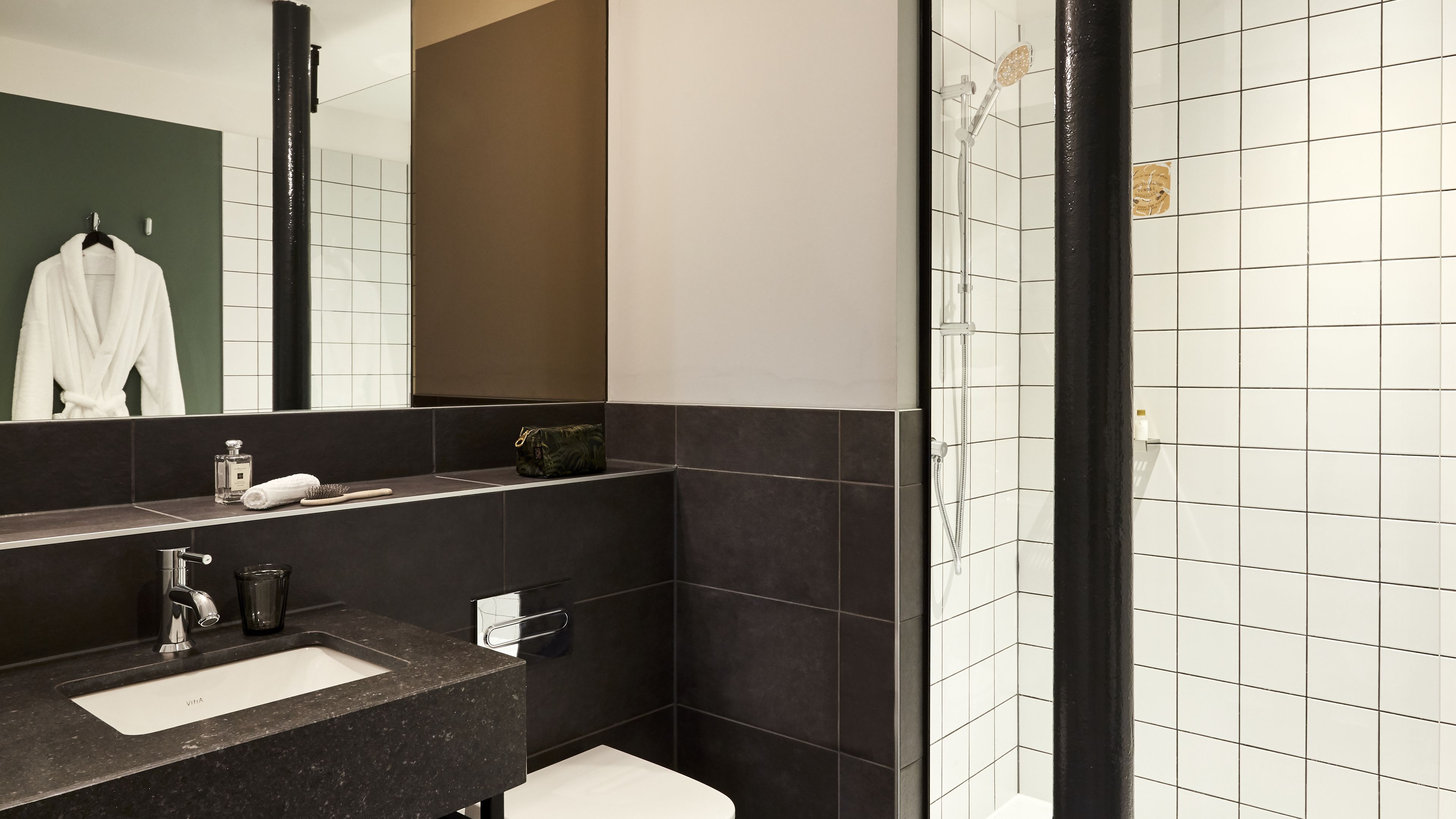 Un baño moderno con lavamanos de superficie oscura, un espejo y zona de ducha.