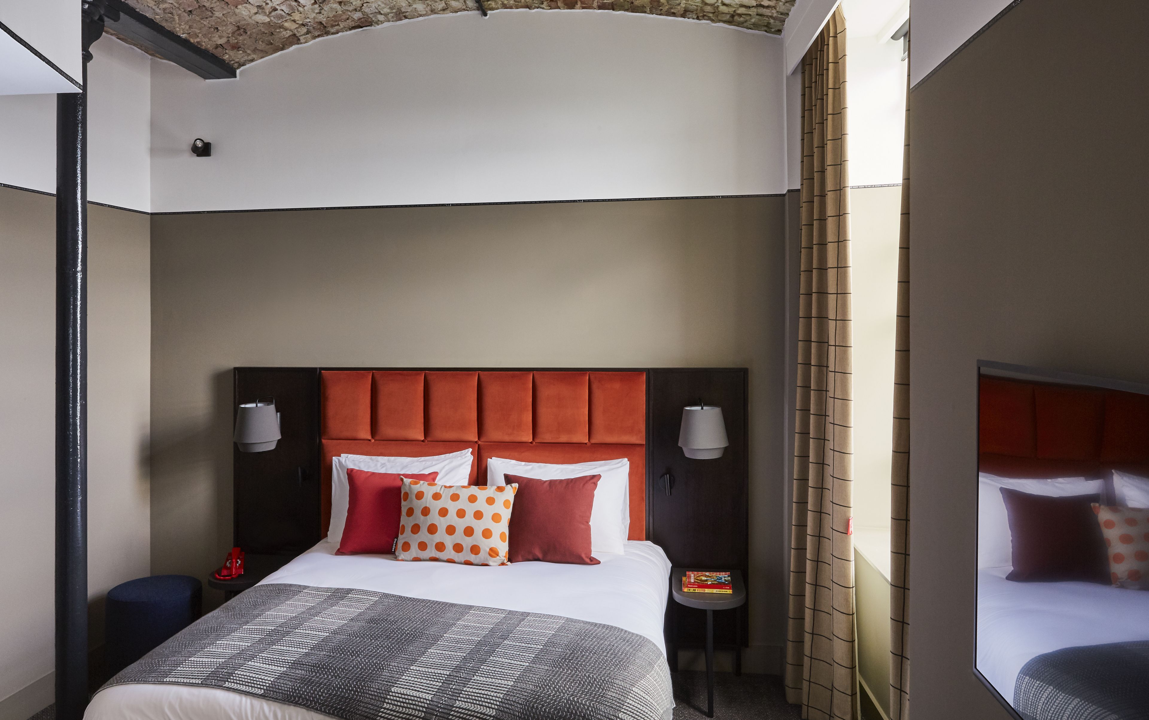 A hotel room with a large bed, a headboard, two bedside lamps, a small table, and a nightstand.