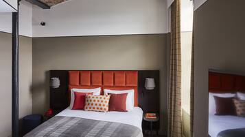 A hotel room with a large bed, a headboard, two bedside lamps, a small table, and a nightstand.