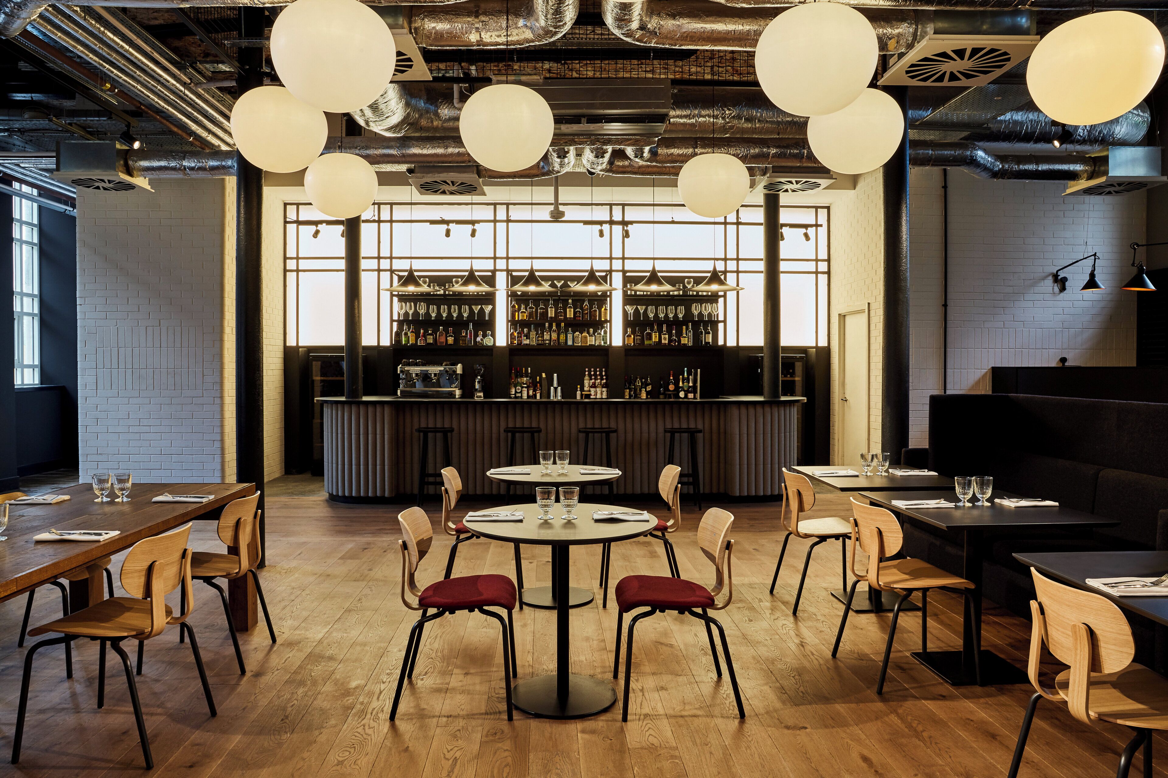 A modern bar area with round tables, bar stools, and a variety of bottles and glasses on shelves.